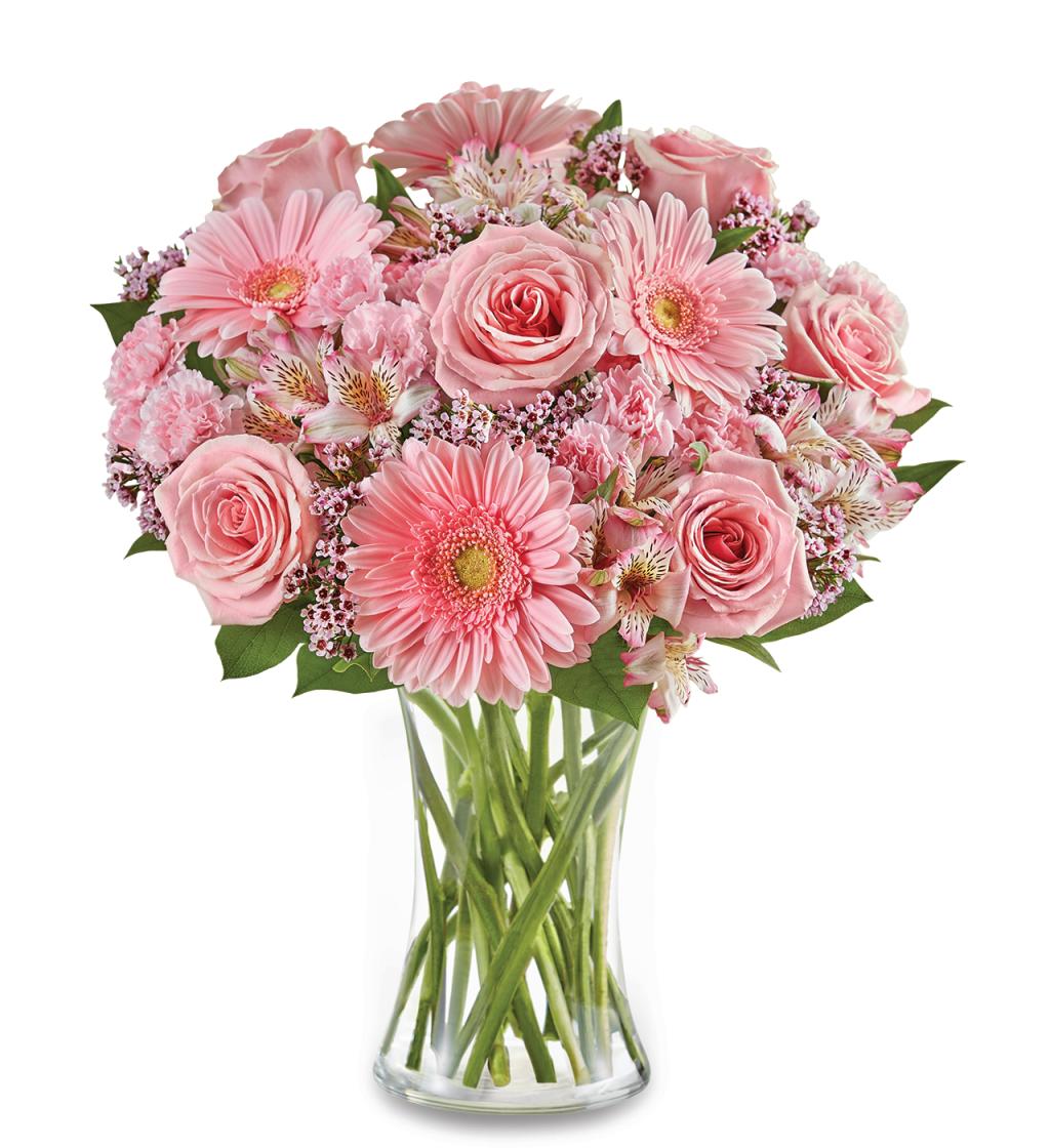 The For All She Does Bouquet by Fleuriste Terrafolia Flowers features pink roses, gerbera daisies, and assorted blooms with lush greens in a clear glass vase, beautifully displayed against a white background.