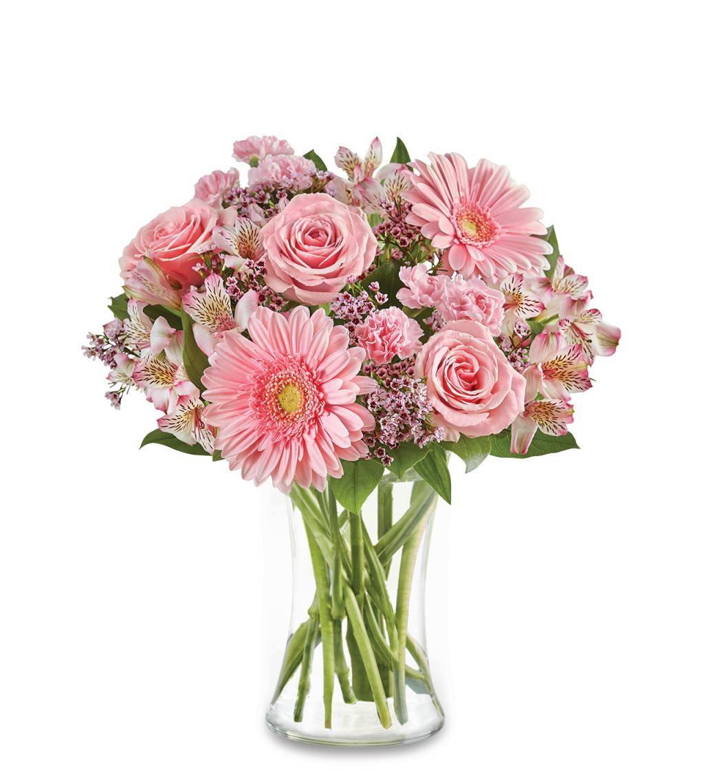 The For All She Does Bouquet by Fleuriste Terrafolia Flowers features pink roses, gerbera daisies, and assorted blooms with lush greens in a clear glass vase, beautifully displayed against a white background.