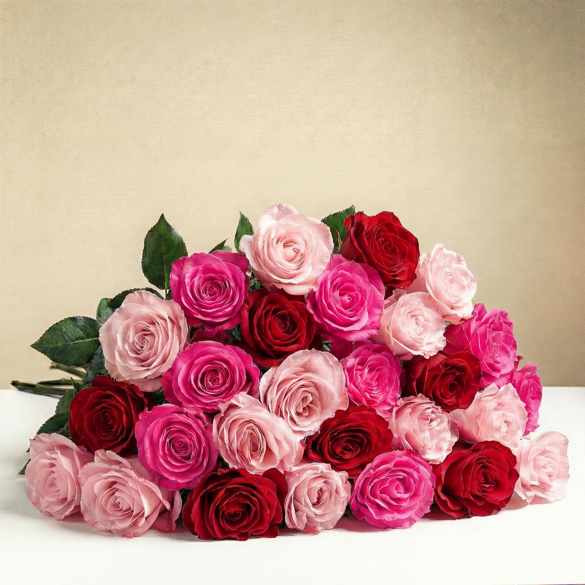 The TF True Romance Roses Wrapped features fresh pink and red roses with vibrant green stems and leaves, beautifully arranged on a white surface against a beige background.