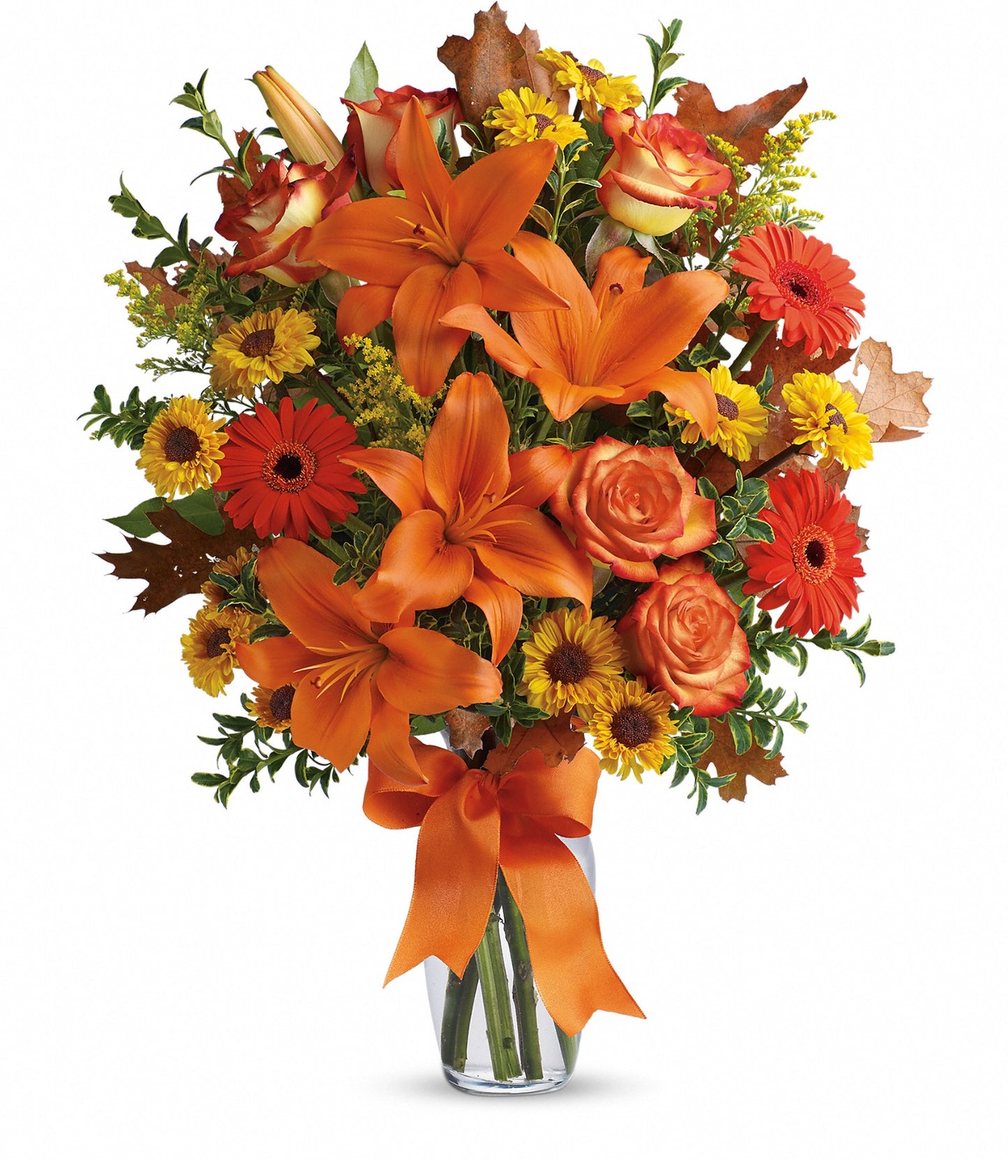 The Burst of Autumn by TF features a clear glass vase filled with Asiatic lilies, red roses, yellow daisies, autumn leaves, and an orange ribbon for a vibrant fresh flower display.