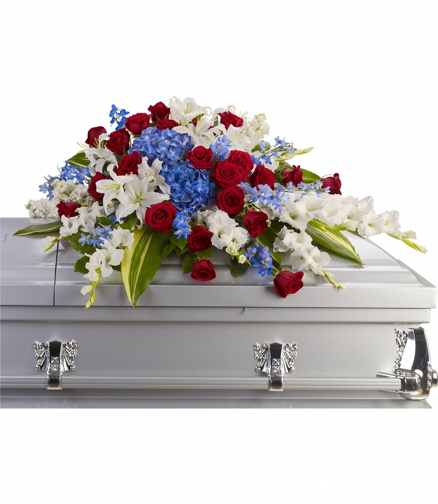 The Distinguished Service Casket Spray features a silver casket adorned with elegant red roses, vibrant blue hydrangea, white oriental lilies, and lush greenery.