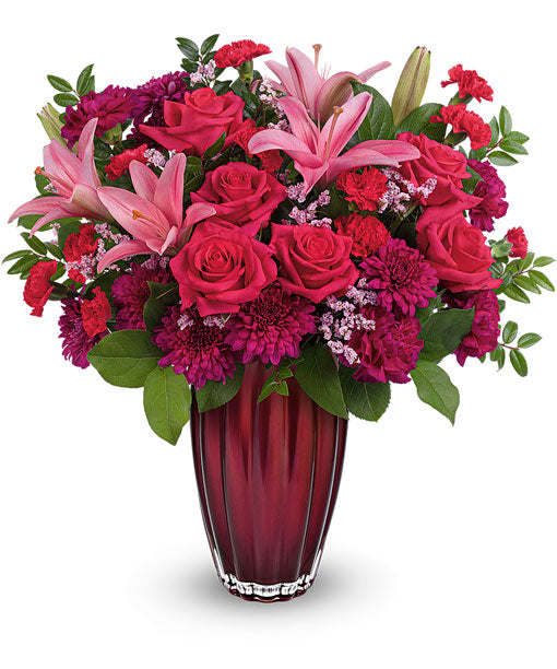 The TF Modern Devotion Bouquet features pink asiatic lilies, hot pink roses, magenta carnations, purple chrysanthemums, and green leaves in a vibrant arrangement.