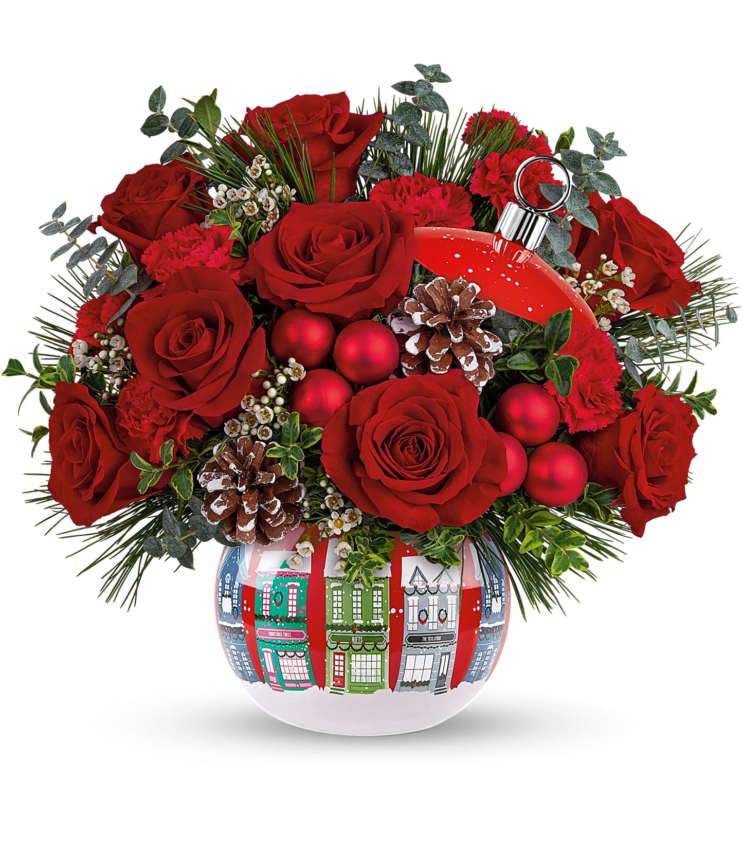 The Snowy Village Bouquet features red roses, miniature carnations, pinecones, greenery, and red ornaments in a white vase with Christmas houses plus a Snowy Village Ornament—perfect for festive decorating.