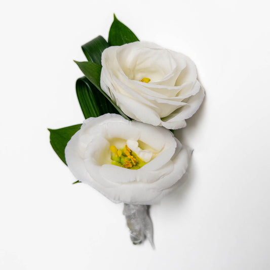 The Noble Stem Boutonniere features two white lisianthus blooms with yellow centers and green leaves, elegantly arranged—an ideal accessory for formal events—shown against a plain white background.