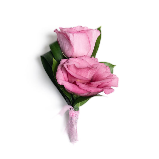 The Velvet Honor Boutonniere features two pink lisianthus flowers with green leaves, tied with a light pink ribbon against a white background—an elegant choice for formal events.