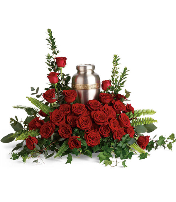 The Forever In Our Hearts Cremation Tribute by Fleuriste Terrafolia Flowers features a silver urn surrounded by red roses, greenery, and fern leaves—an elegant arrangement ideal for memorials or funerals.