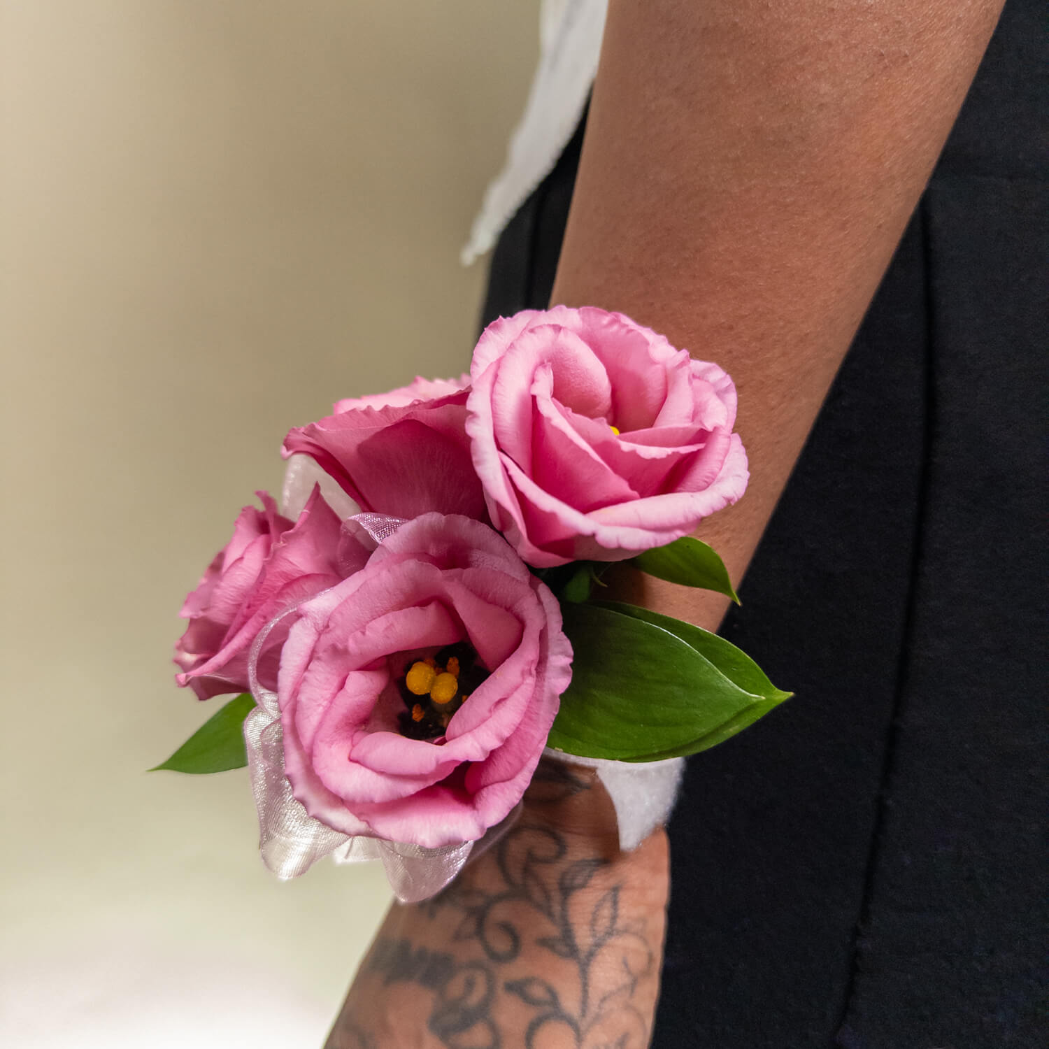 Le bracelet Blush Bloom présente trois roses roses avec des feuilles vertes et un ruban blanc transparent, disposées simplement pour une touche d'élégance - parfait pour les mariages ou les bals de fin d'année.