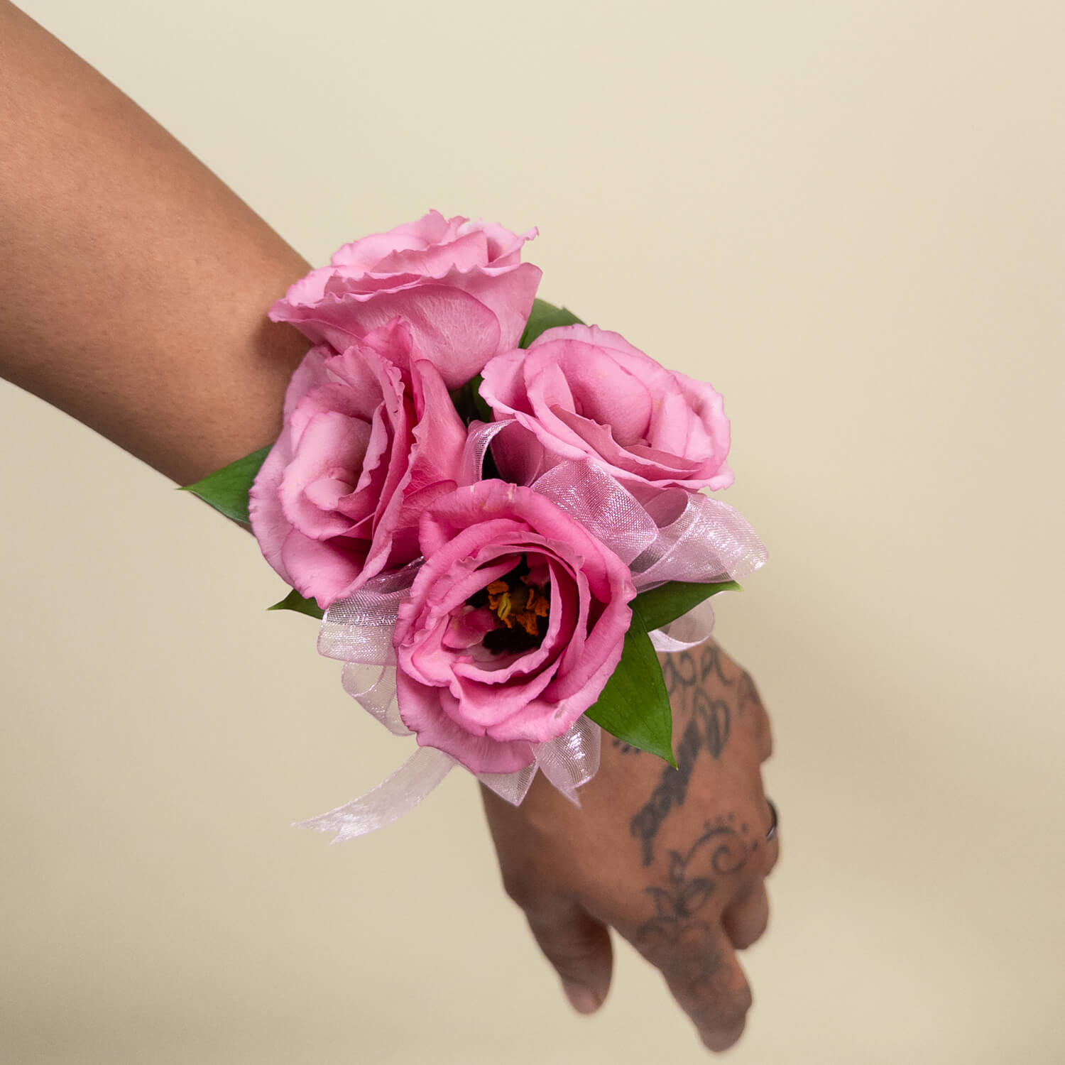 Le bracelet Blush Bloom présente trois roses roses avec des feuilles vertes et un ruban blanc transparent, disposées simplement pour une touche d'élégance - parfait pour les mariages ou les bals de fin d'année.