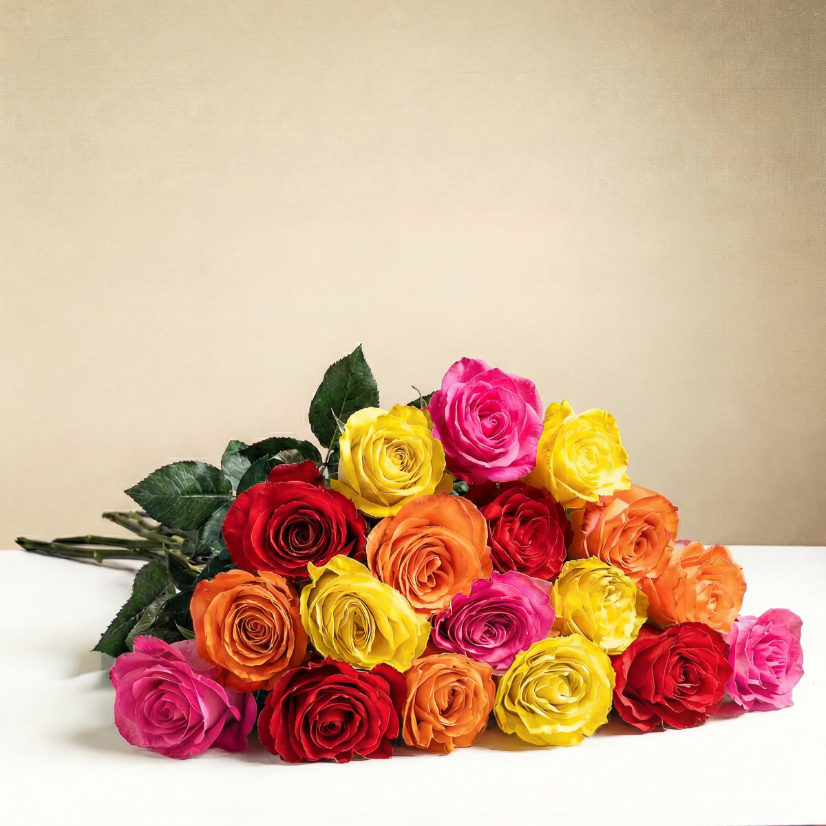 The TF Bright Spark Roses Wrapped features a romantic bouquet of vibrant pink, yellow, orange, and red roses arranged on a white surface with a plain beige background.