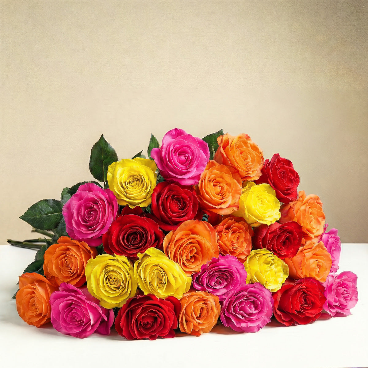 The TF Bright Spark Roses Wrapped features a romantic bouquet of vibrant pink, yellow, orange, and red roses arranged on a white surface with a plain beige background.