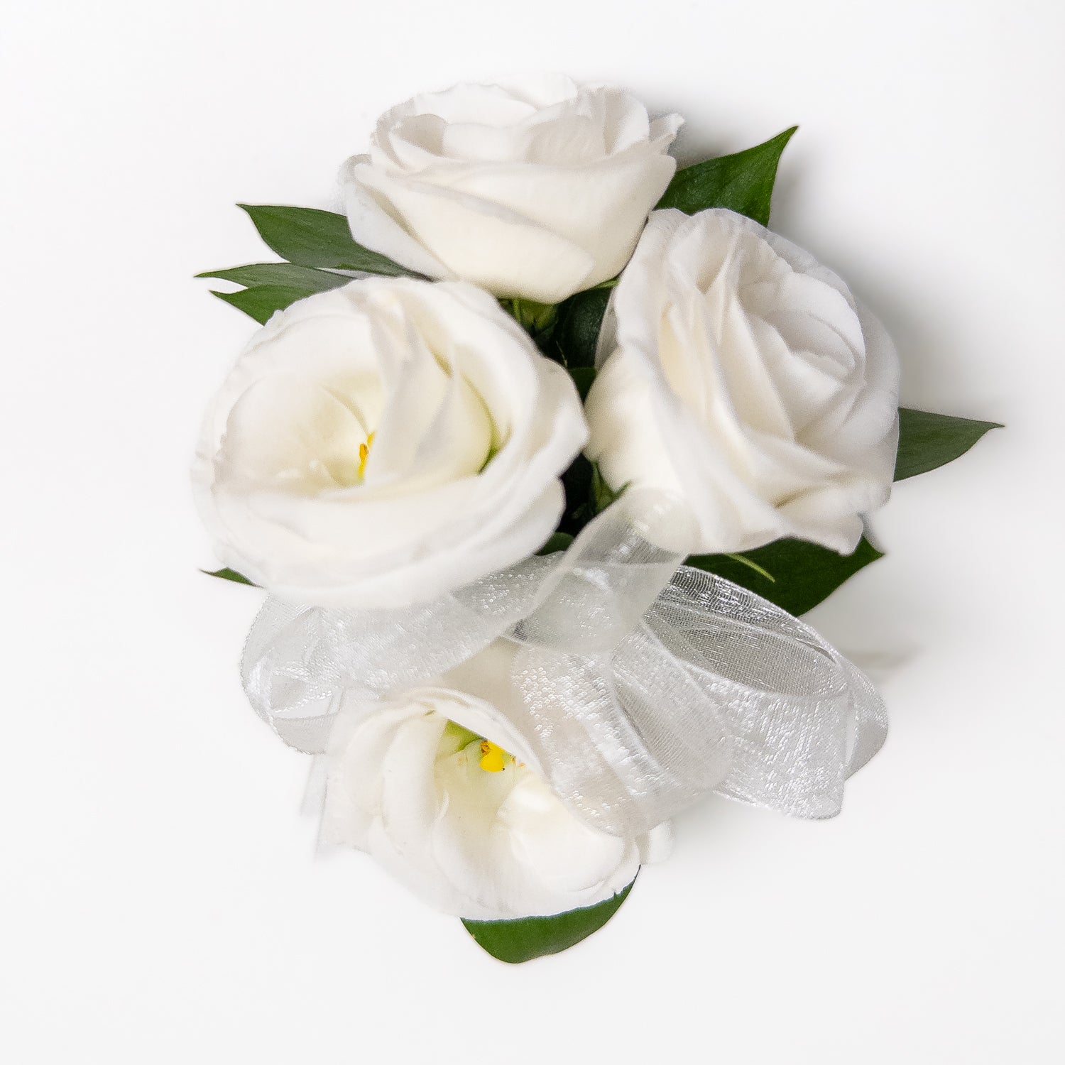 The White Muse Wristlet features three hand-crafted white roses with green leaves, tied with a sheer white ribbon—an elegant accessory perfect for weddings or formal occasions. Displayed on a white background.