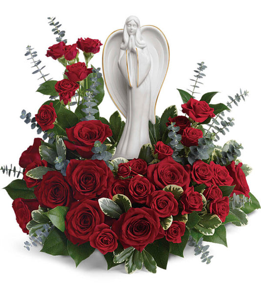 The Forever Our Angel Bouquet by Fleuriste Terrafolia Flowers features a white angel keepsake surrounded by red roses, eucalyptus, and lush greenery for an elegant and striking floral display.