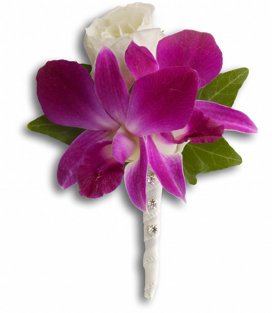 The Fresh in Fuchsia Boutonniere by TF features a large purple dendrobium orchid and white rose, accented with lush ivy and green leaves, all wrapped in white ribbon with rhinestone details.