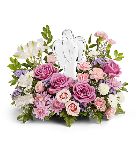 The In Heaven's Arms Bouquet features a crystal angel keepsake surrounded by lavender roses, pink carnations, white lilies, chrysanthemums, and lush greenery for a peaceful, elegant display.