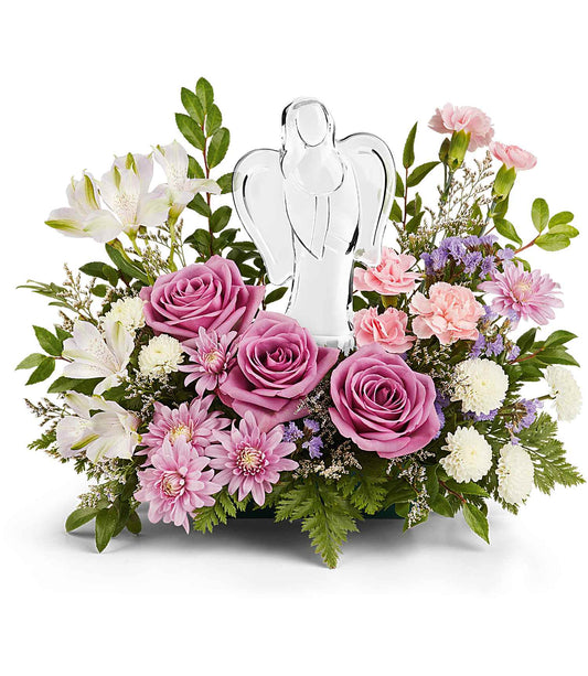 The In Heaven's Arms Bouquet features a crystal angel keepsake surrounded by lavender roses, pink carnations, white lilies, chrysanthemums, and lush greenery for a peaceful, elegant display.
