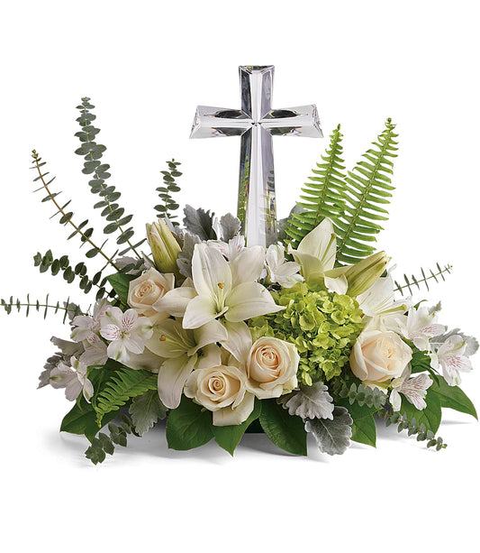 The Life's Glory Bouquet features crème roses, green hydrangea, white lilies, ferns, and assorted greenery, artfully arranged around a Large Crystal Cross Keepsake.