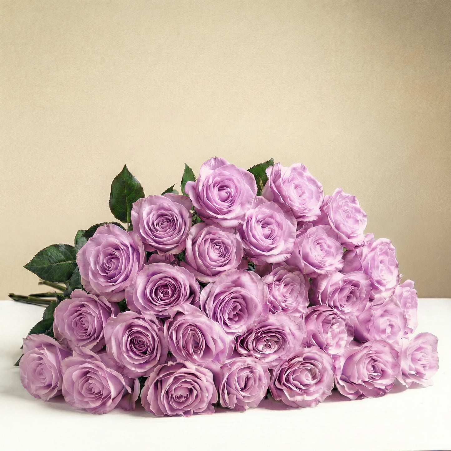 The TF Long Stem Lavender Roses Wrapped features twelve romantic lavender roses with green stems and leaves, elegantly arranged on a white surface set against a beige background.