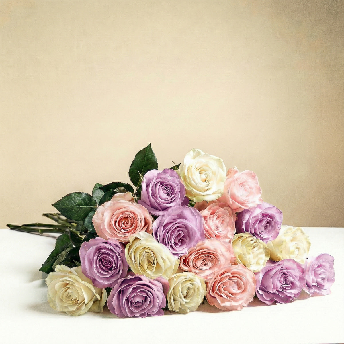 The TF Long Stem Pastel Roses Wrapped features white, pink, and lavender roses with visible green stems and leaves, beautifully arranged on a white surface with a beige background for a romantic touch.