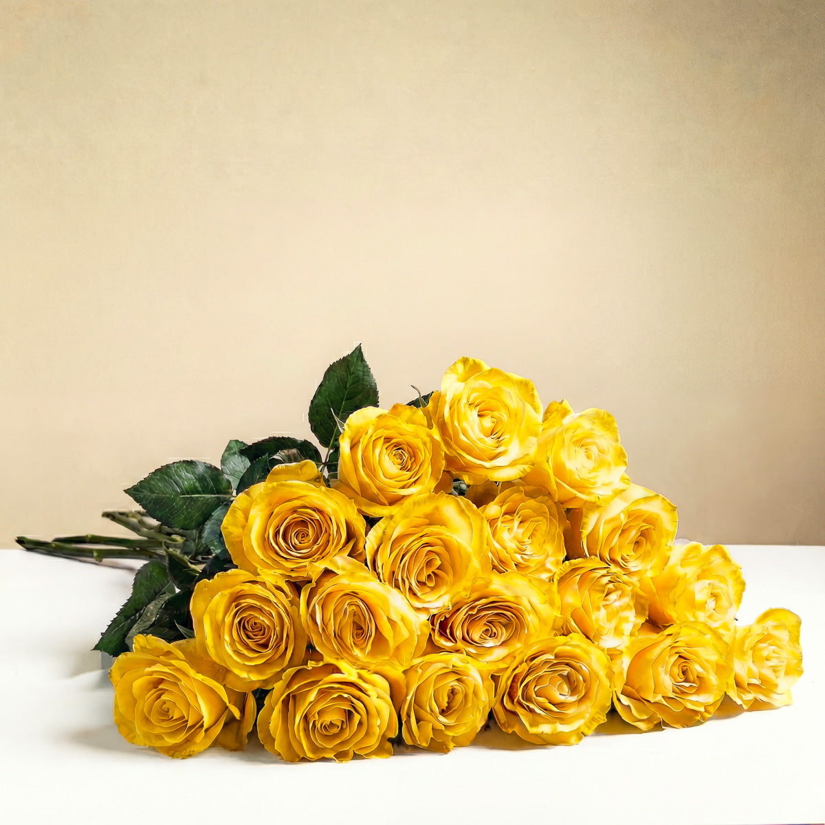 The TF Long Stem Yellow Roses Wrapped bouquet, featuring vibrant yellow roses with green stems, is displayed on a white surface with a plain beige background.