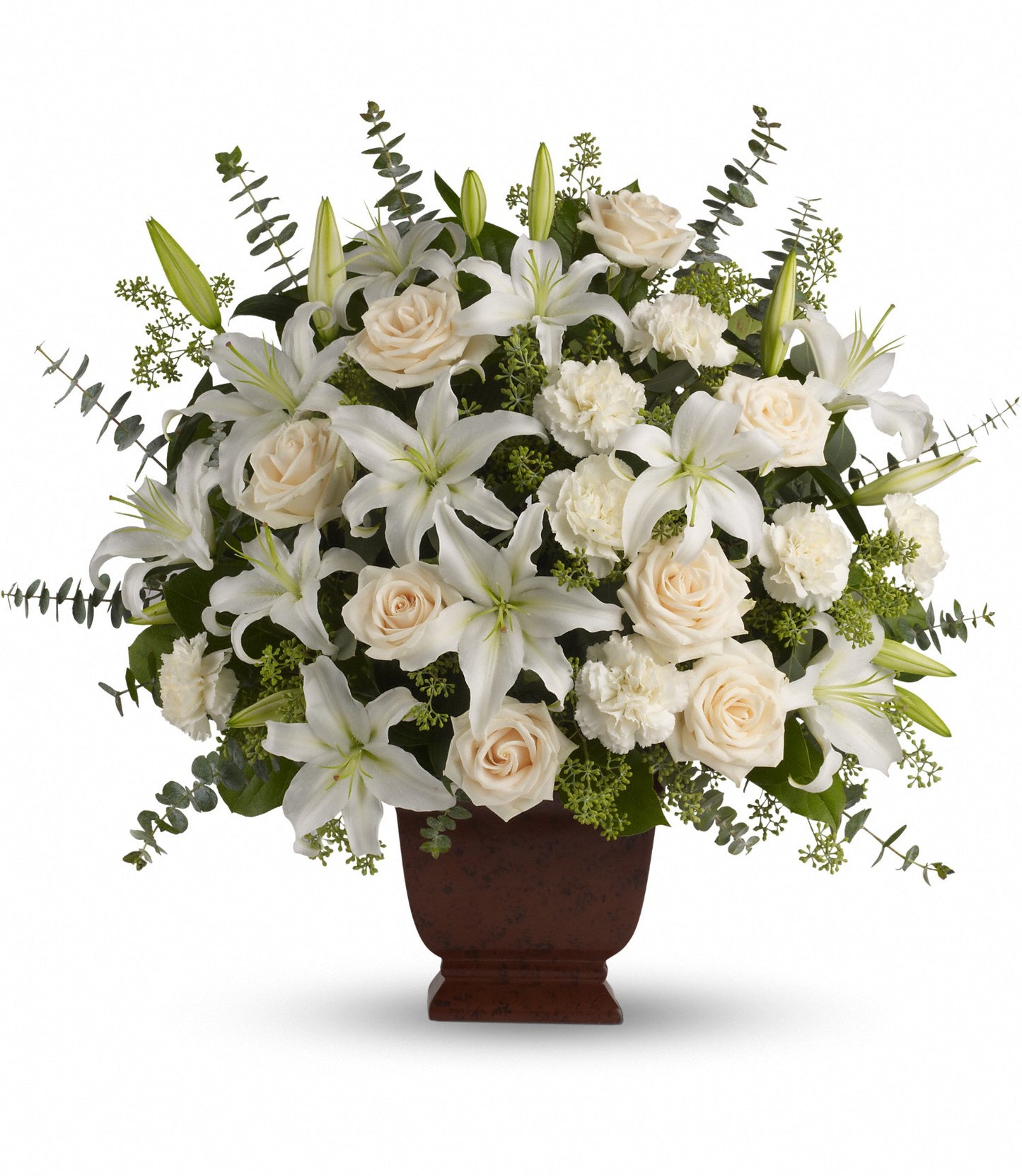 The TF Loving Lilies and Roses bouquet features white oriental lilies, crème roses, and carnations with green foliage and eucalyptus leaves in a brown vase against a plain background.