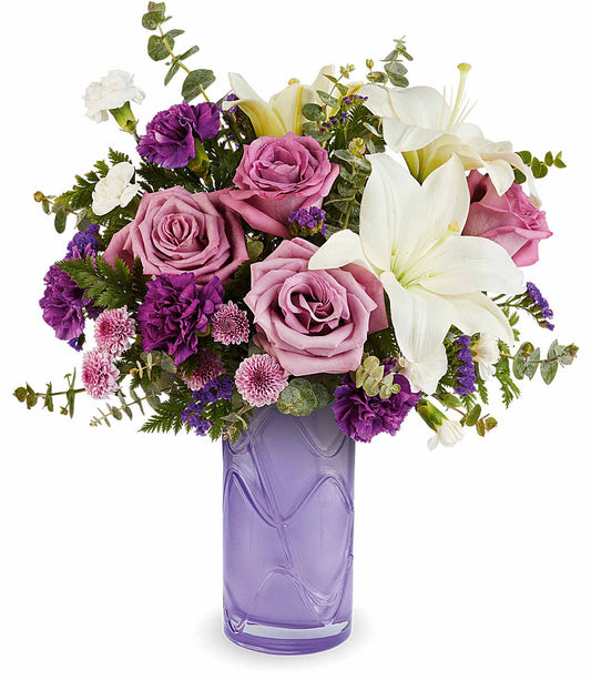 The Mauvelous Bloom Bouquet features pink and lavender roses, white asiatic lilies, purple carnations, and assorted greenery for a lush, elegant display perfect for any occasion.