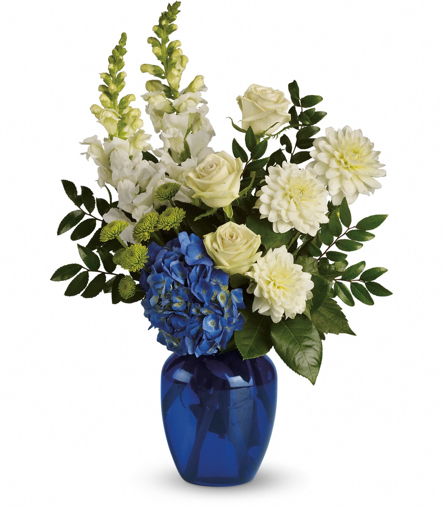 The Ocean Devotion bouquet features white dahlias, snapdragons, green roses, blue hydrangea, and button poms in a shiny blue glass vase with lush greenery.