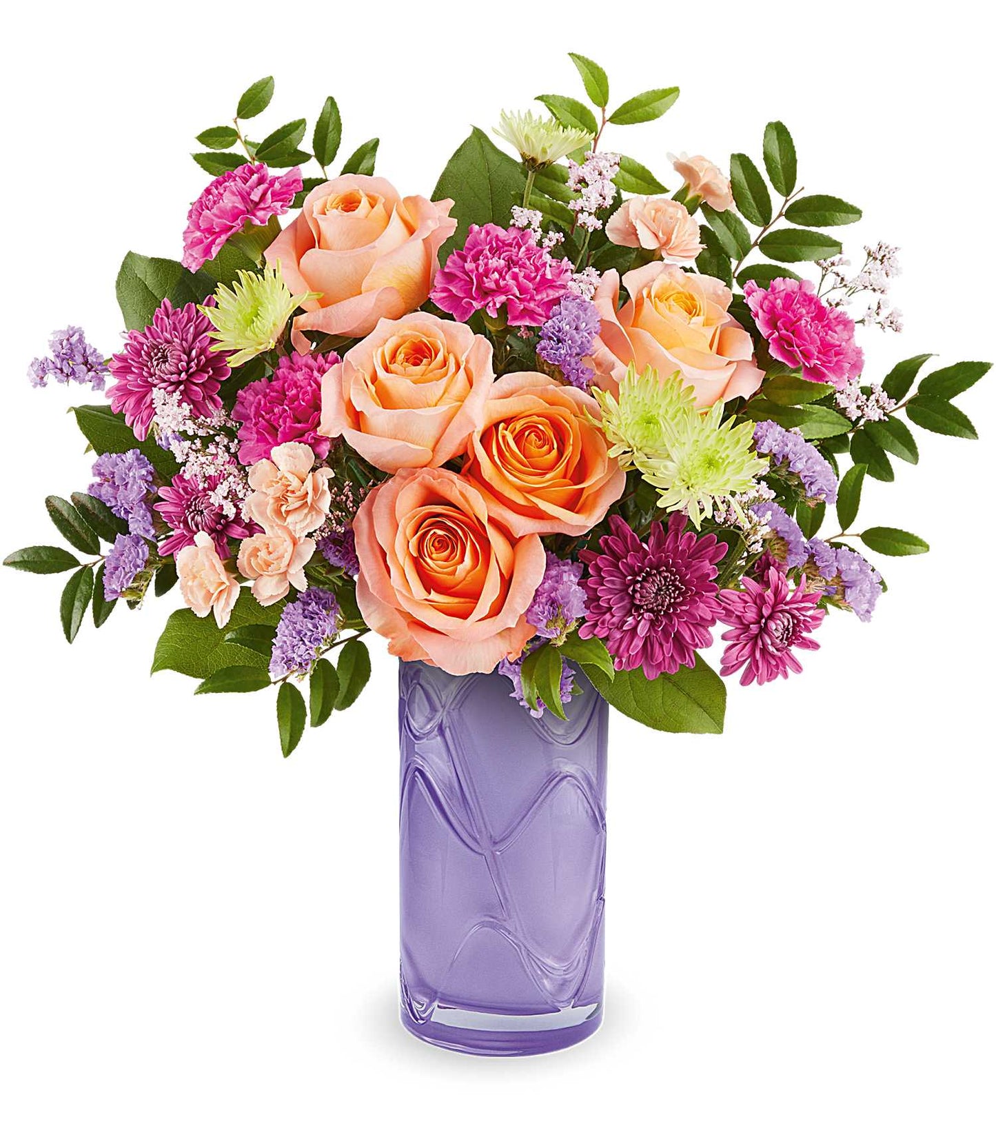 The Pretty Daydream Bouquet features fuchsia carnations, peach roses, and purple blooms with green leaves in a tall, textured vase.