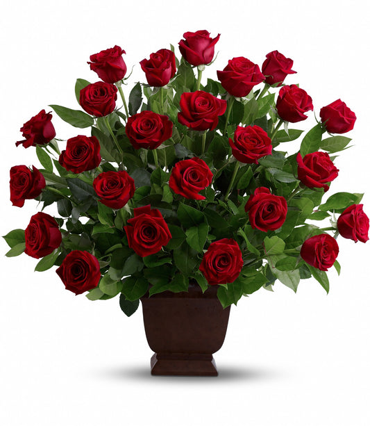 The Rose Tribute Bouquet features vibrant red roses and lush salal leaves elegantly arranged in a dark brown Noble Heritage Urn, presented against a plain white background.