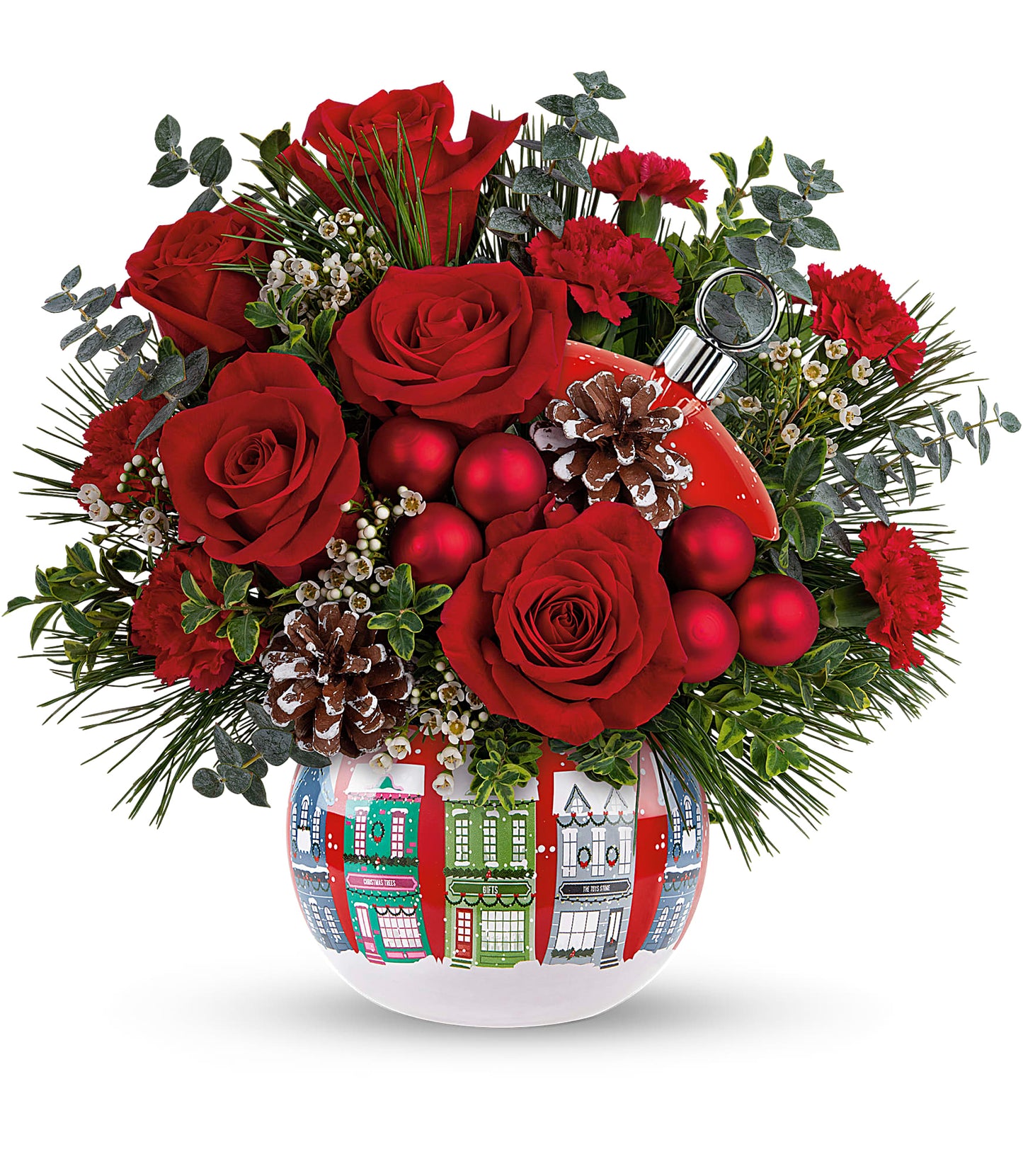 The Snowy Village Bouquet features red roses, miniature carnations, pinecones, greenery, and red ornaments in a white vase with Christmas houses plus a Snowy Village Ornament—perfect for festive decorating.