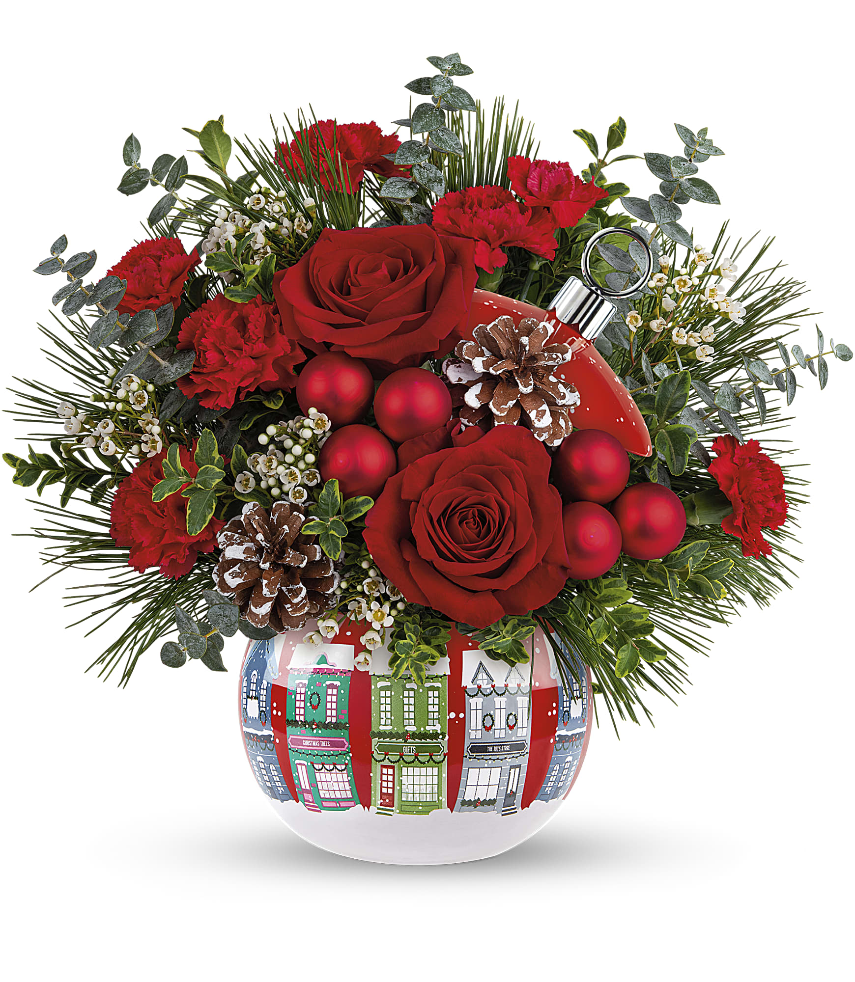 The Snowy Village Bouquet features red roses, miniature carnations, pinecones, greenery, and red ornaments in a white vase with Christmas houses plus a Snowy Village Ornament—perfect for festive decorating.