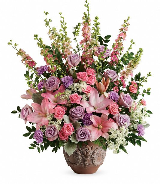 The Soft Blush Bouquet features a decorative ceramic vase filled with pink asiatic lilies, pink and lavender roses, purple carnations, and greenery for an elegant, colorful touch.